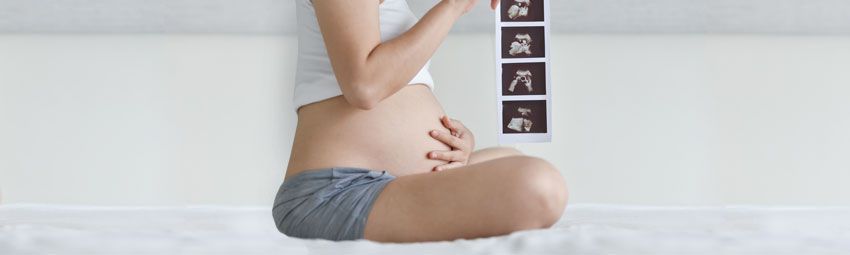 Femme enceinte assise en tailleur, une main sur le ventre, l'autre tenant une échographie